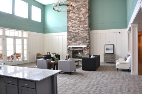 The Hendrickson community room with a two-story ceiling, stone fireplace, and tall windows